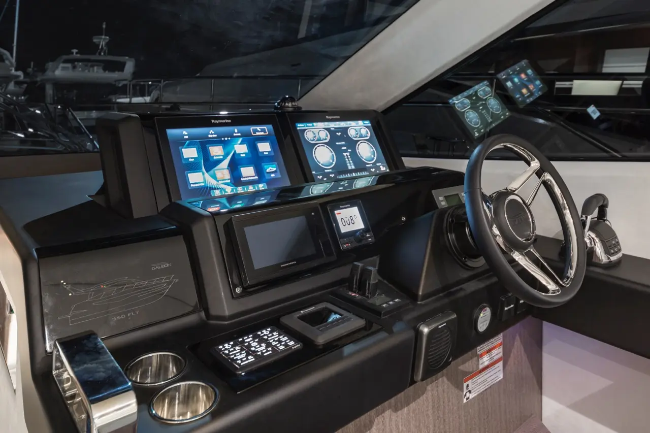 Modern yacht control panel featuring multiple screens, steering wheel, and navigation instruments, with 'Raymarine' displayed.