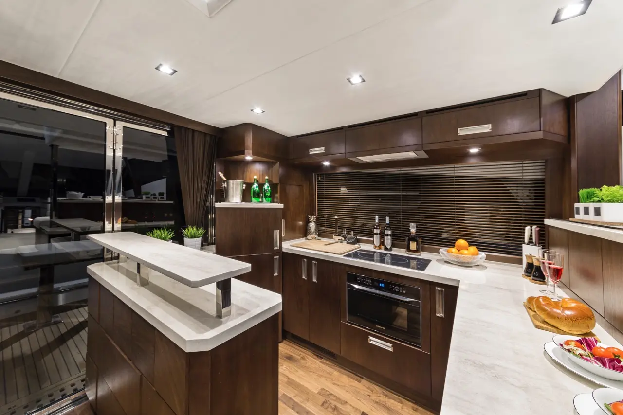 Modern yacht kitchen featuring dark wood cabinetry, stainless appliances, and decorative elements including fruits and drinks.
