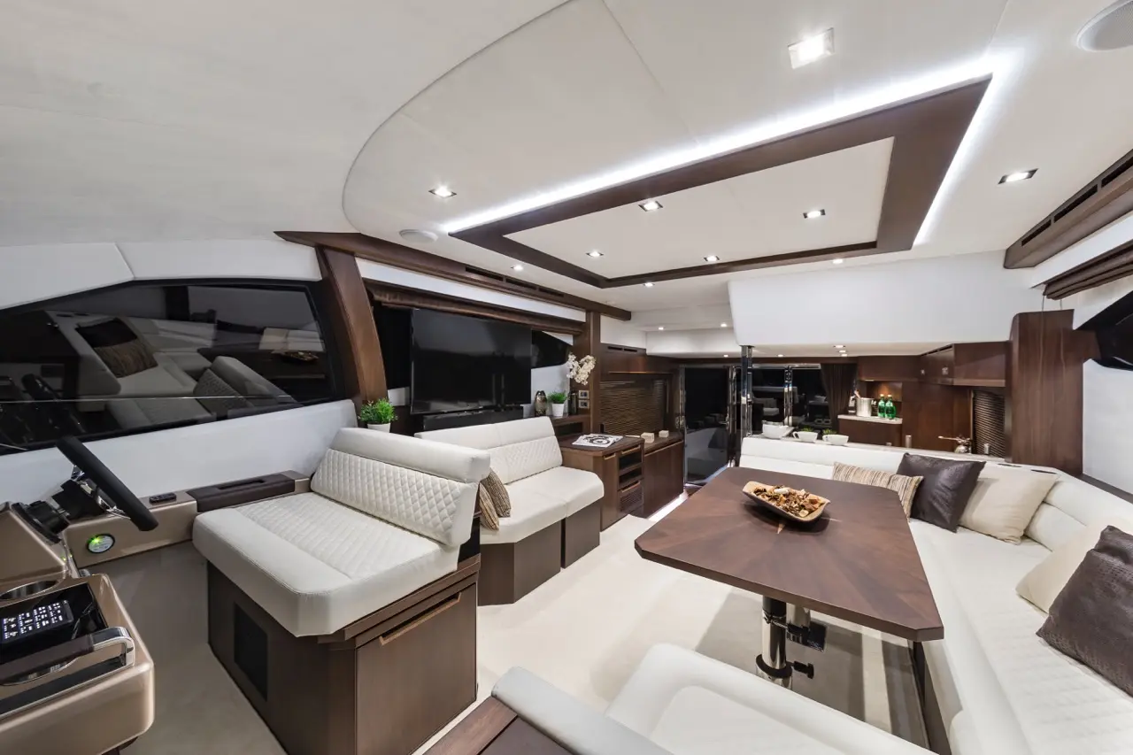 Modern yacht interior featuring plush seating, a dining table, helm station, and ambient lighting, with a TV display visible.