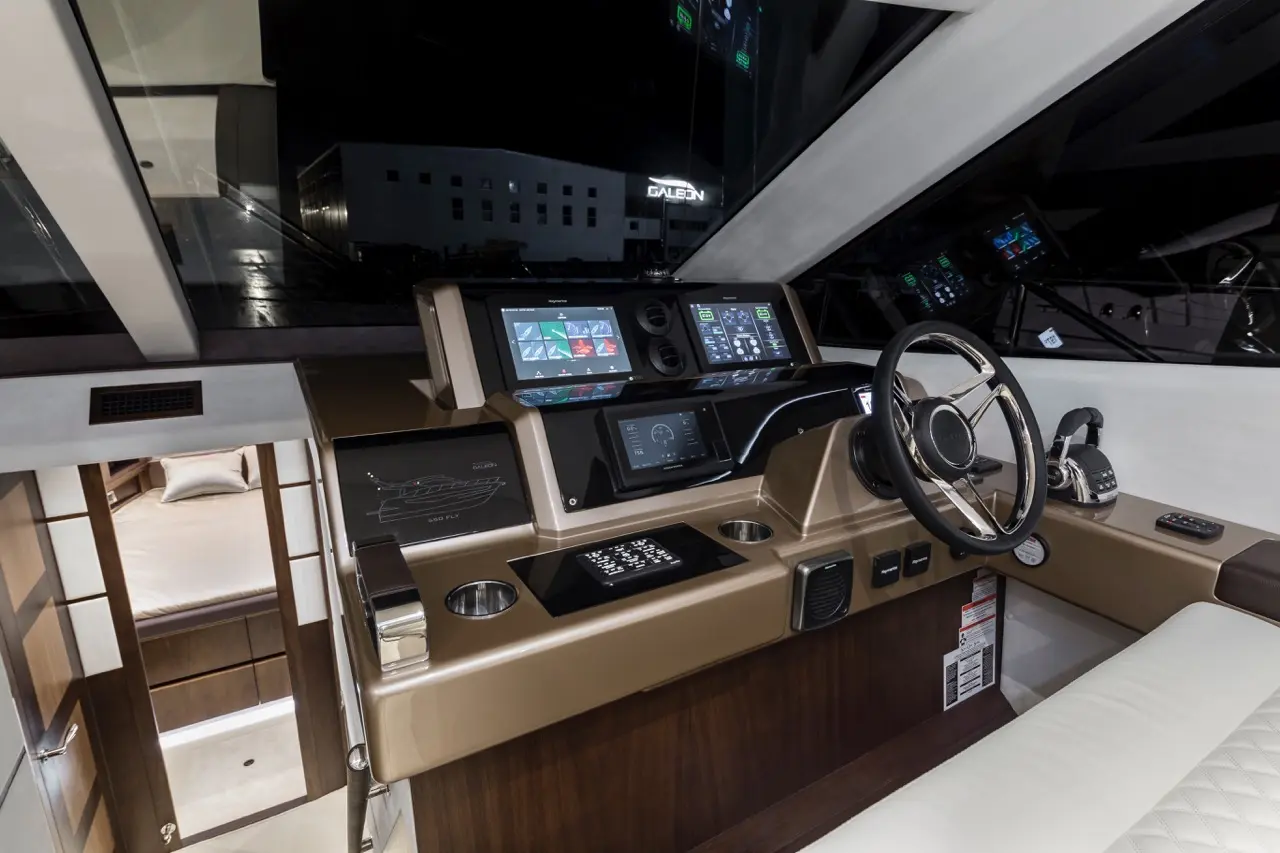 Modern yacht cockpit featuring dual touchscreen displays, steering wheel, and helm controls, with a view of a cabin entrance.