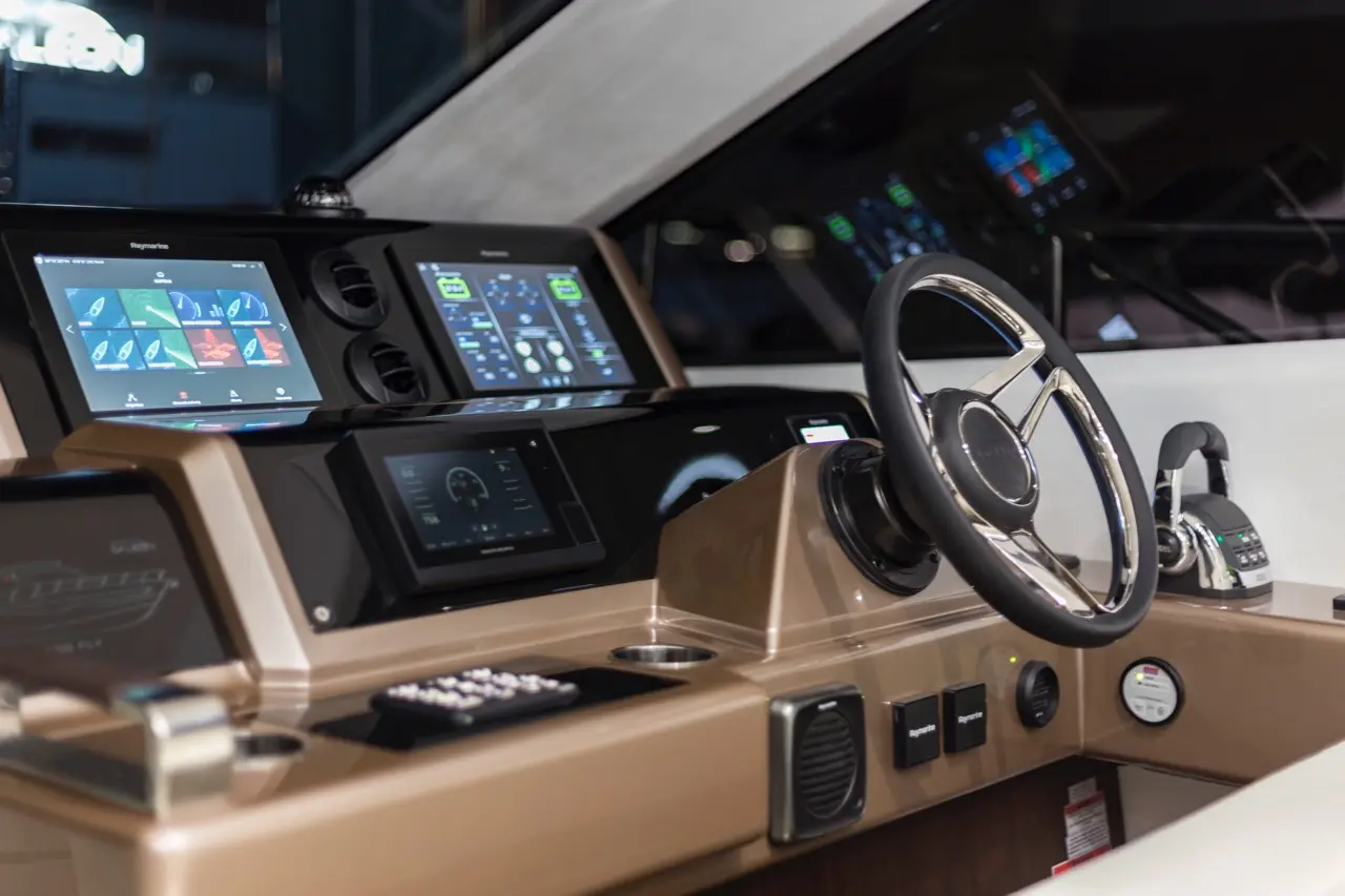 Modern boat dashboard featuring digital screens, a steering wheel, and control buttons, showcasing navigation equipment and design.