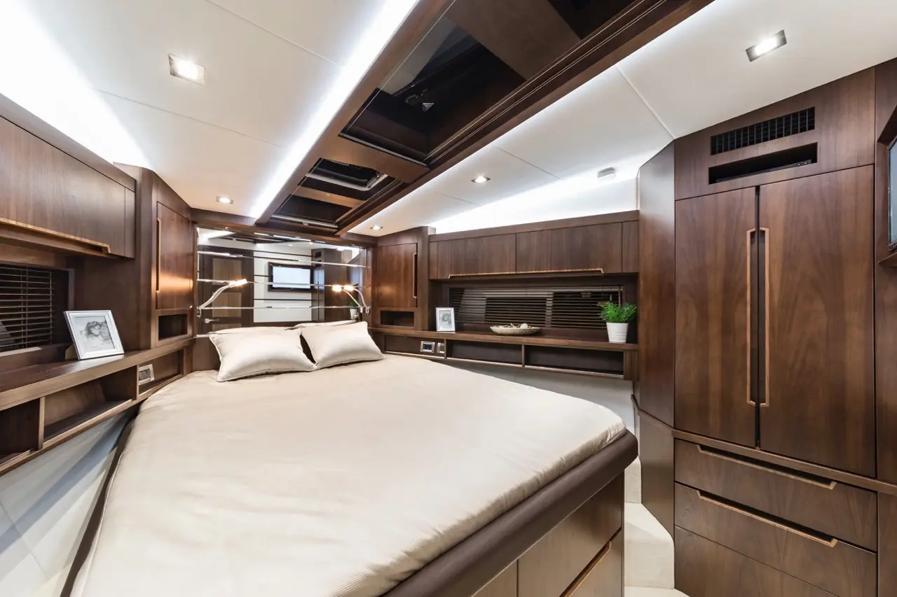 Modern yacht bedroom with a large bed, wooden cabinetry, soft lighting, and a TV mounted on the wall. Cozy and elegant design.