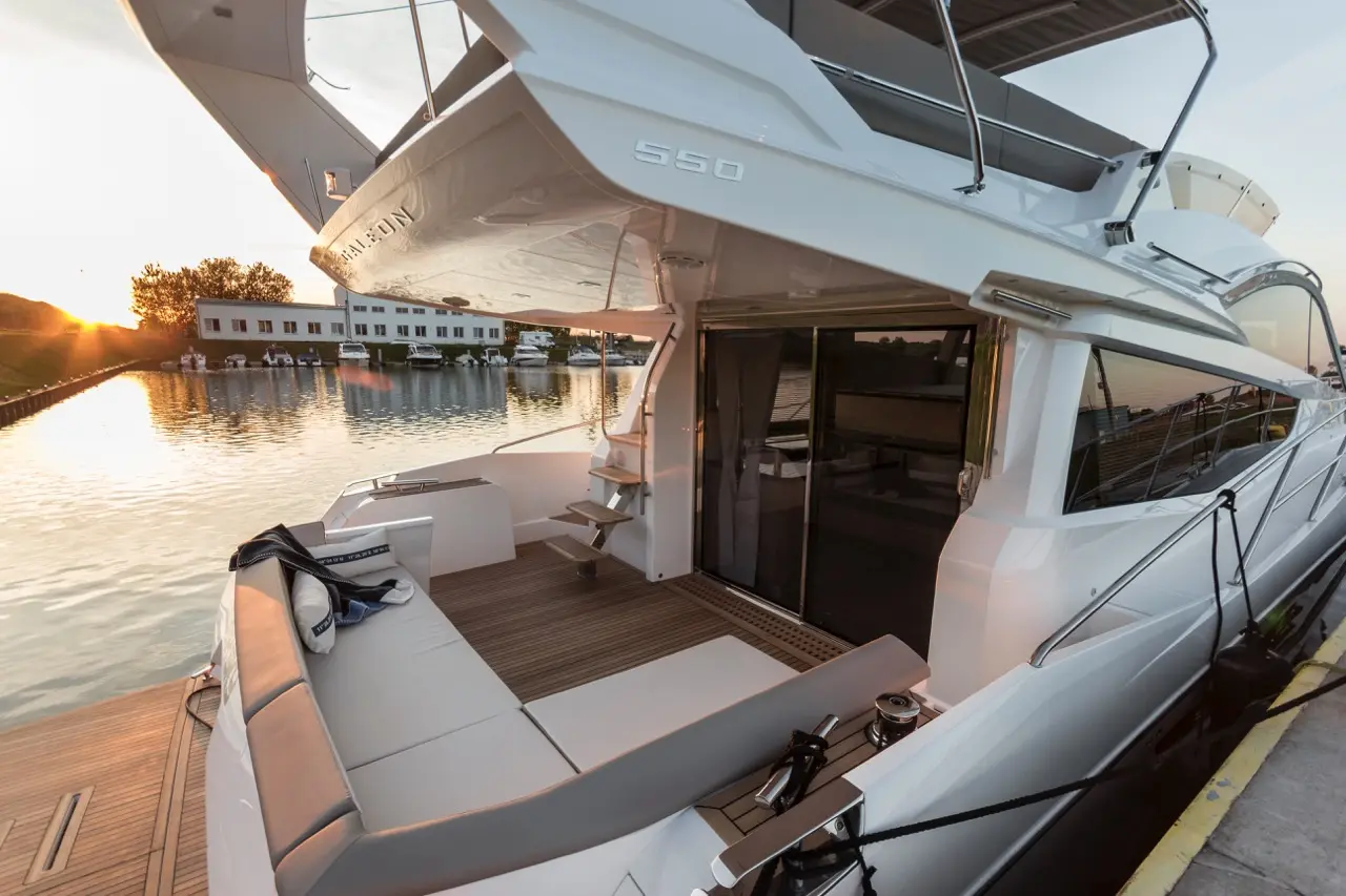 Luxurious yacht 550 docked at sunset, showcasing a spacious deck with seating, steps, and reflections on calm water.