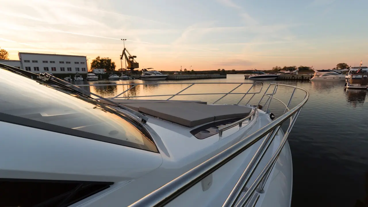 A luxury yacht moored at a marina during sunset, with calm waters reflecting a colorful sky and nearby boats.