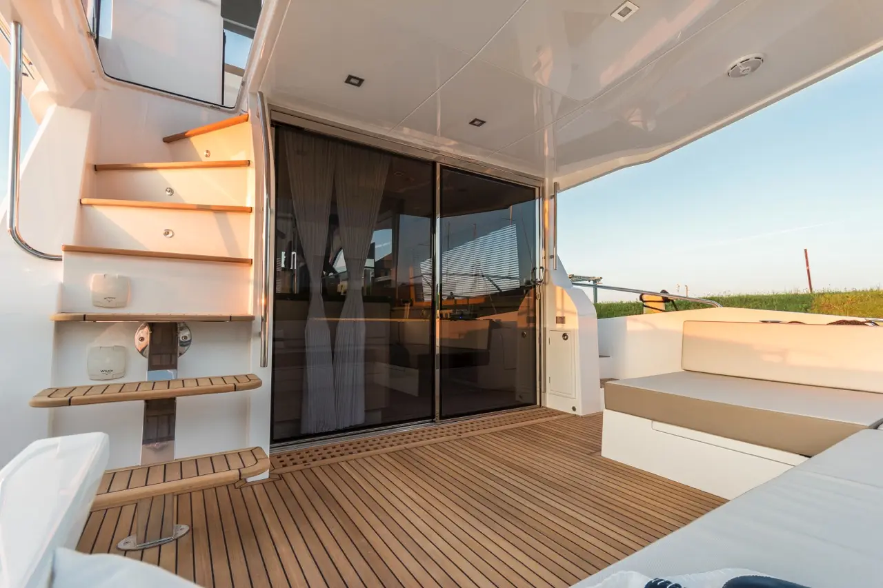 Modern boat deck with wooden stairs leading to an interior, featuring glass doors and a spacious seating area.