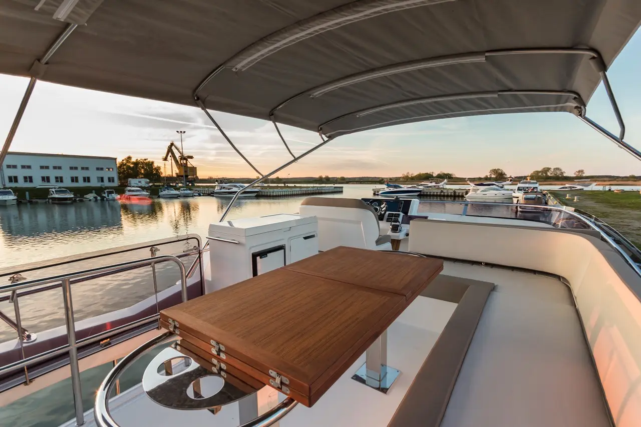A luxurious boat deck with a wooden table, overlooking a marina at sunset, surrounded by various parked boats.