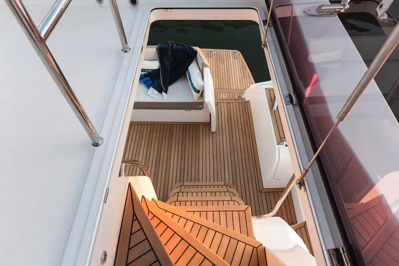 Aerial view of a yacht interior featuring wooden decking, a staircase, and a white seating area with a navy blanket.