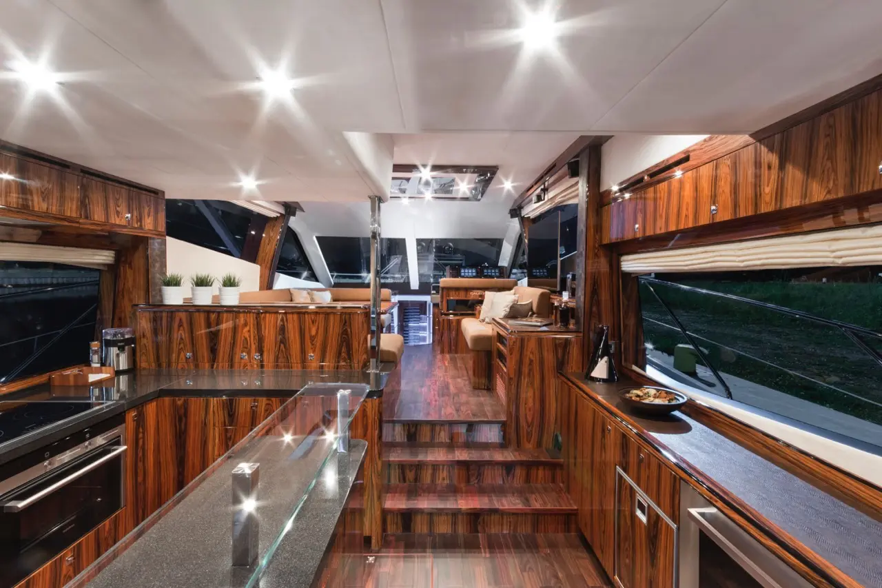 Interior of a luxury yacht featuring sleek wooden cabinetry, modern kitchen appliances, and cozy seating area with windows.