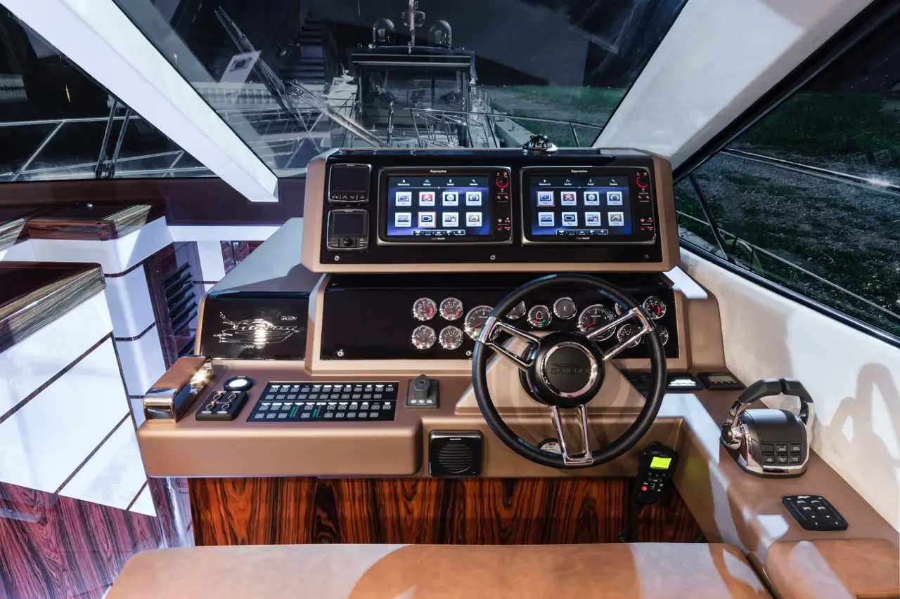 Luxury boat cockpit featuring dual control screens, steering wheel, gauges, and modern navigation equipment.
