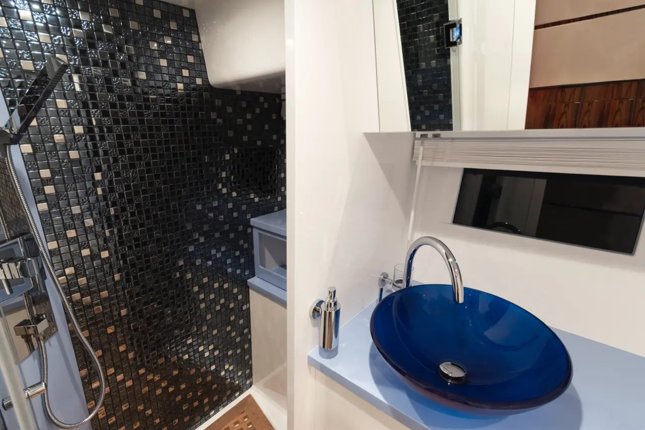 A modern bathroom featuring a blue glass sink, chrome faucet, and a black mosaic tile shower wall.
