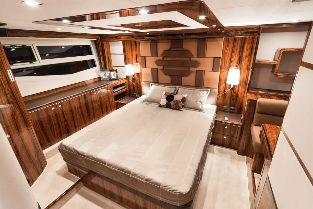 Modern yacht bedroom featuring a king-size bed, wooden accents, and decorative pillows, with ambient lighting and a window view.