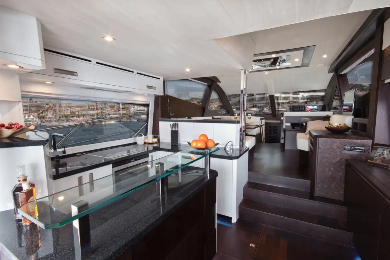 Interior of a luxury yacht featuring a modern kitchen, glass bar, wooden steps, and a view of the marina through large windows.