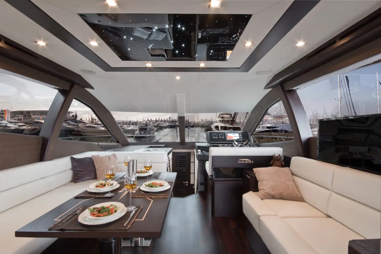 Luxurious yacht interior featuring dining setup with salads, drinks, and a modern helm, showcasing views of the marina.