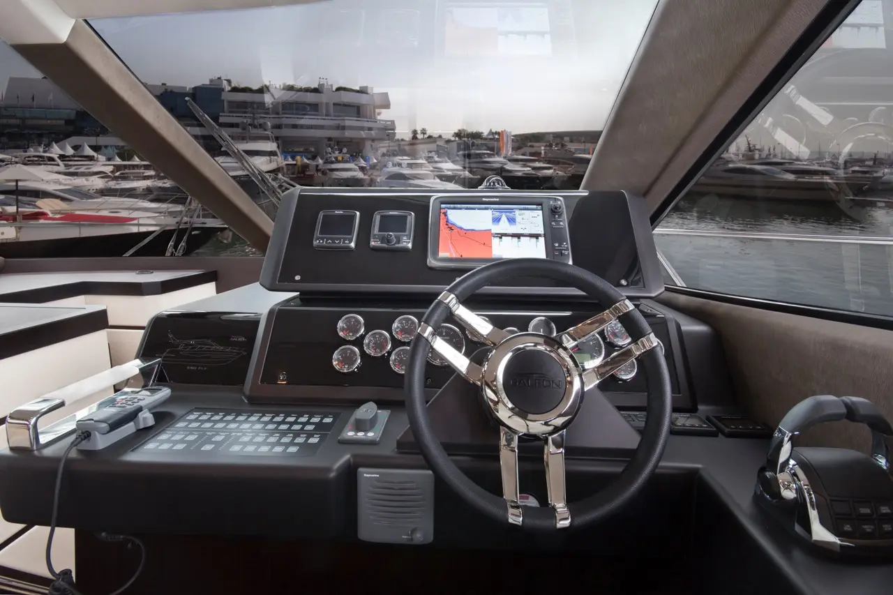 Luxury yacht cockpit with a steering wheel, multiple gauges, and a screen displaying nautical charts.