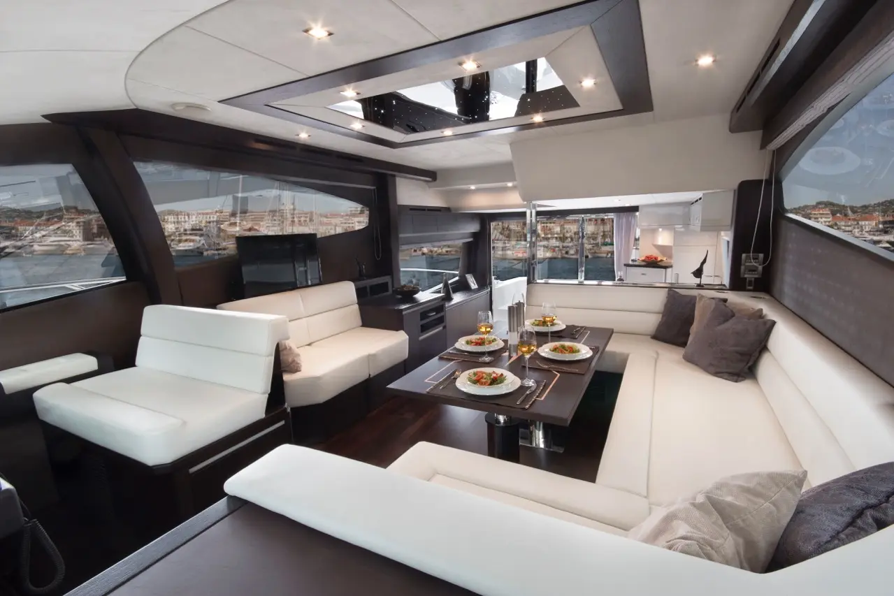 Modern yacht interior featuring a dining table set with food, elegant seats, and panoramic windows overlooking a harbor.