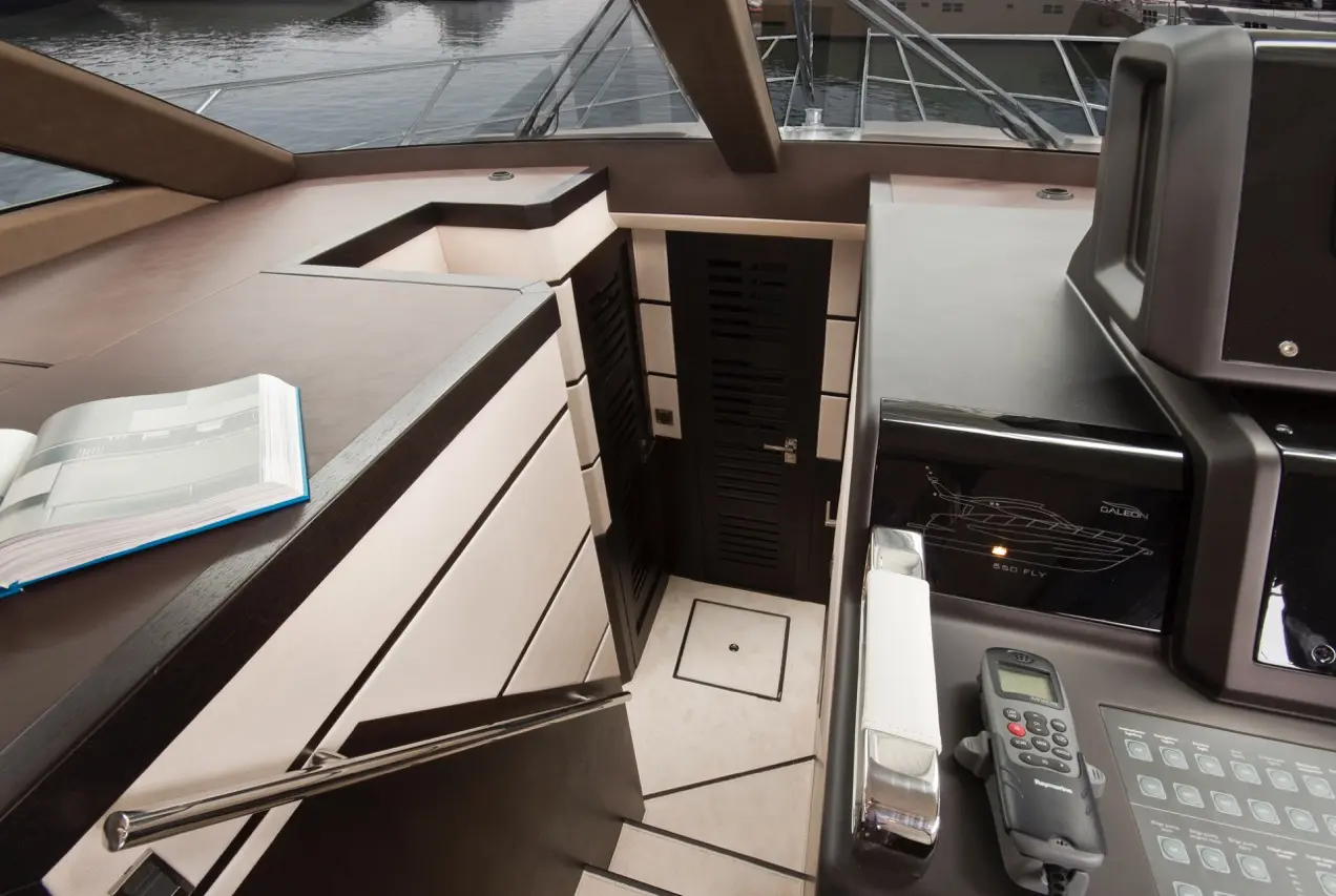 Interior view of a luxury yacht, featuring a navigation area with a remote control, book, and stylish cabinetry.