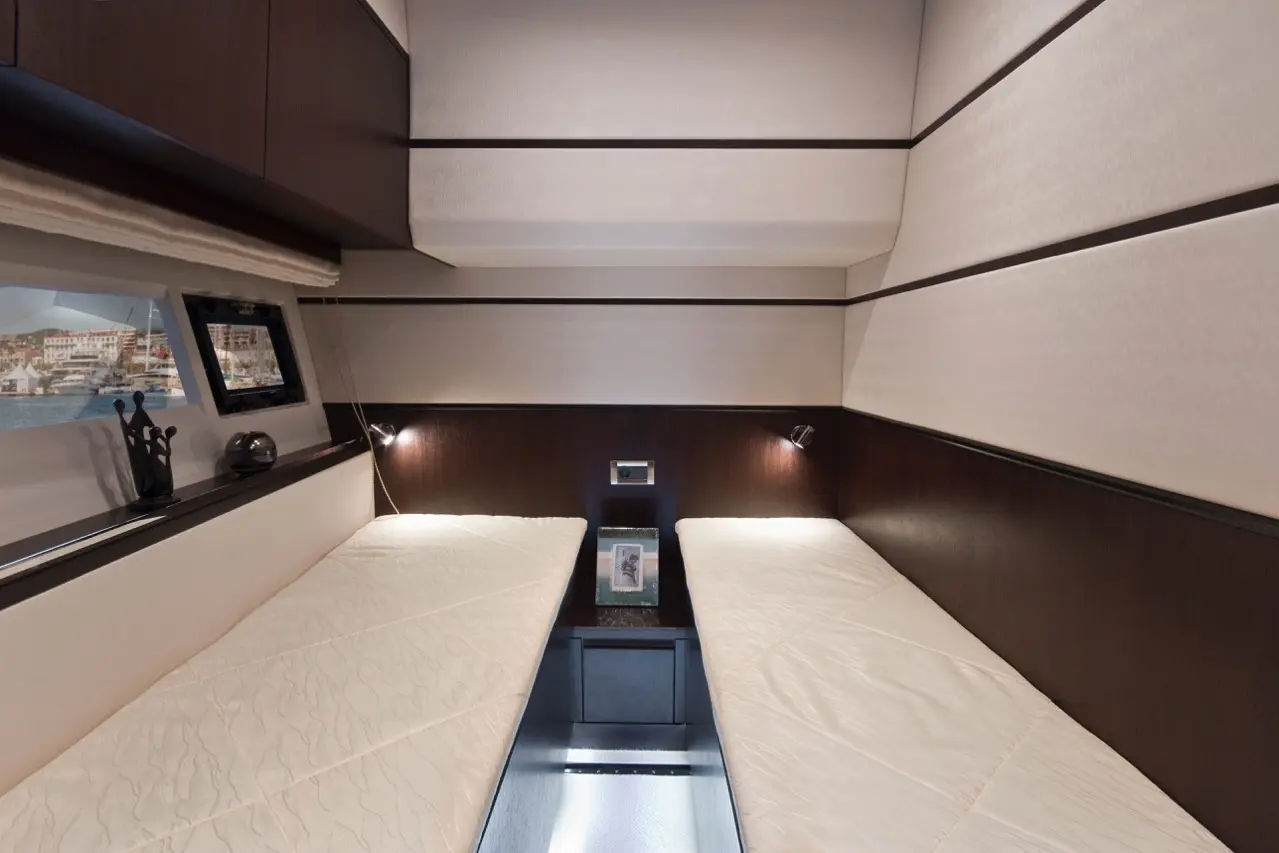 Modern boat cabin featuring two single beds, bedside lamps, a window with a view, and neutral-colored decor.