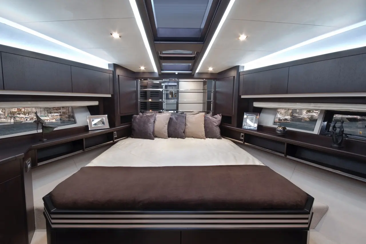 Luxury yacht bedroom featuring a large bed with decorative pillows, modern storage, and a scenic view through windows.