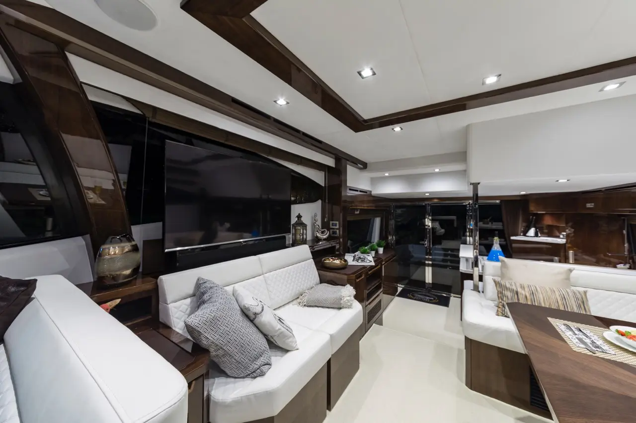 Luxurious yacht interior featuring white couches, a large TV, wooden accents, and a modern dining area with decorative items.