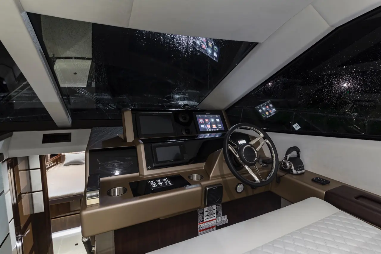 Modern yacht cockpit with digital displays, steering wheel, and rain-streaked windows showing a night scene.