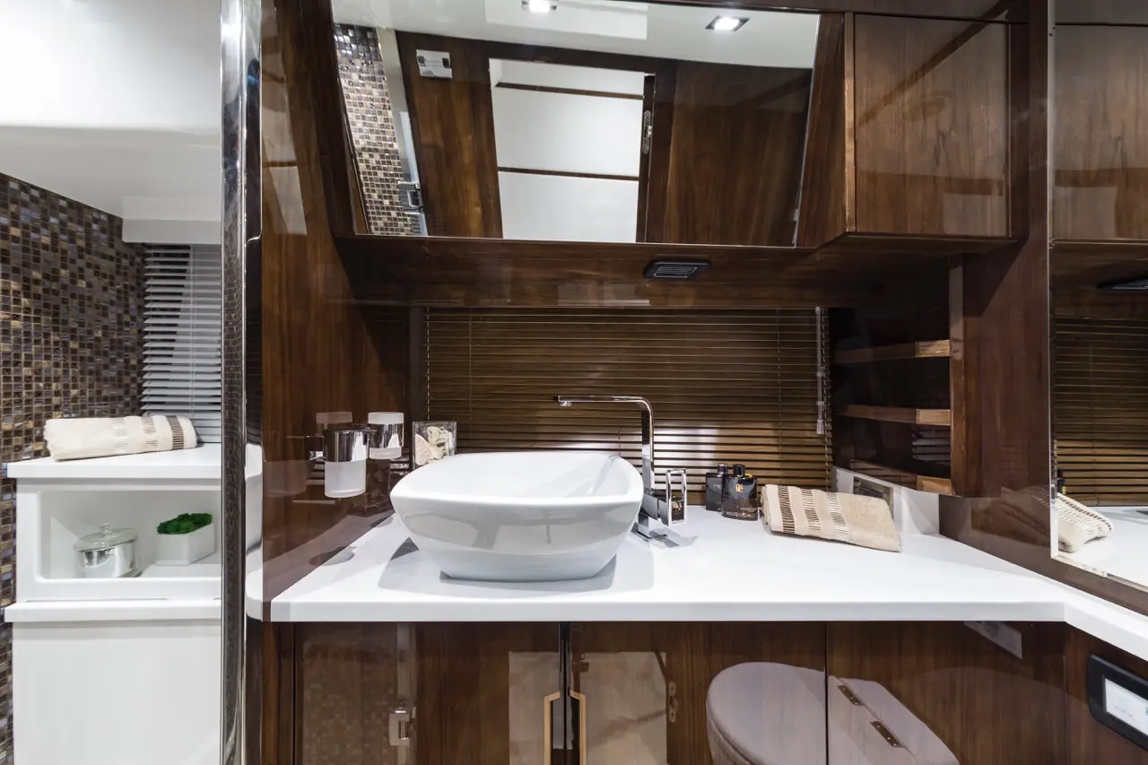 Modern bathroom featuring a stylish white sink, wooden cabinetry, decorative mosaic tiles, and neatly arranged toiletries.