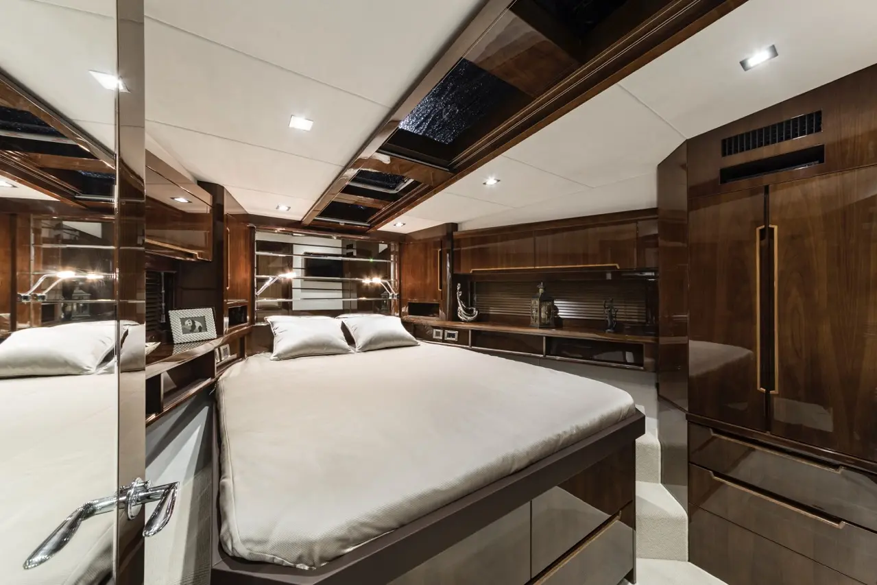 Luxury yacht bedroom featuring a king-sized bed, wooden paneling, and decorative items on shelves with modern lighting.
