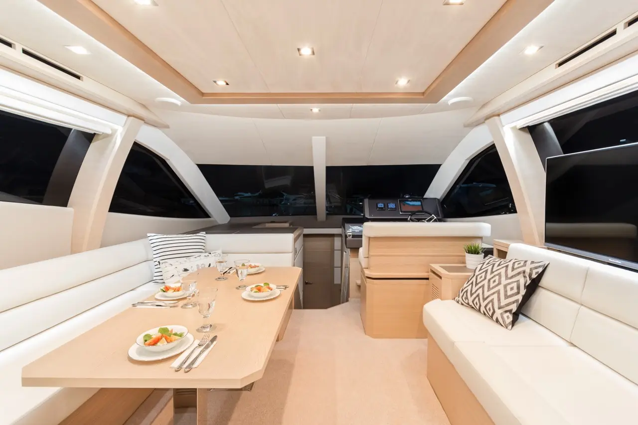 Luxurious yacht interior featuring a dining table with plates of food, sleek seating, and modern control panel at night.