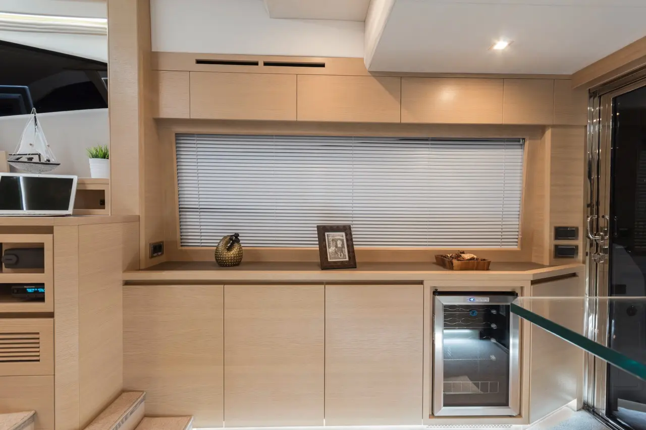 Modern kitchen interior featuring wooden cabinetry, blinds, decorative items, and a wine cooler near a glass table.
