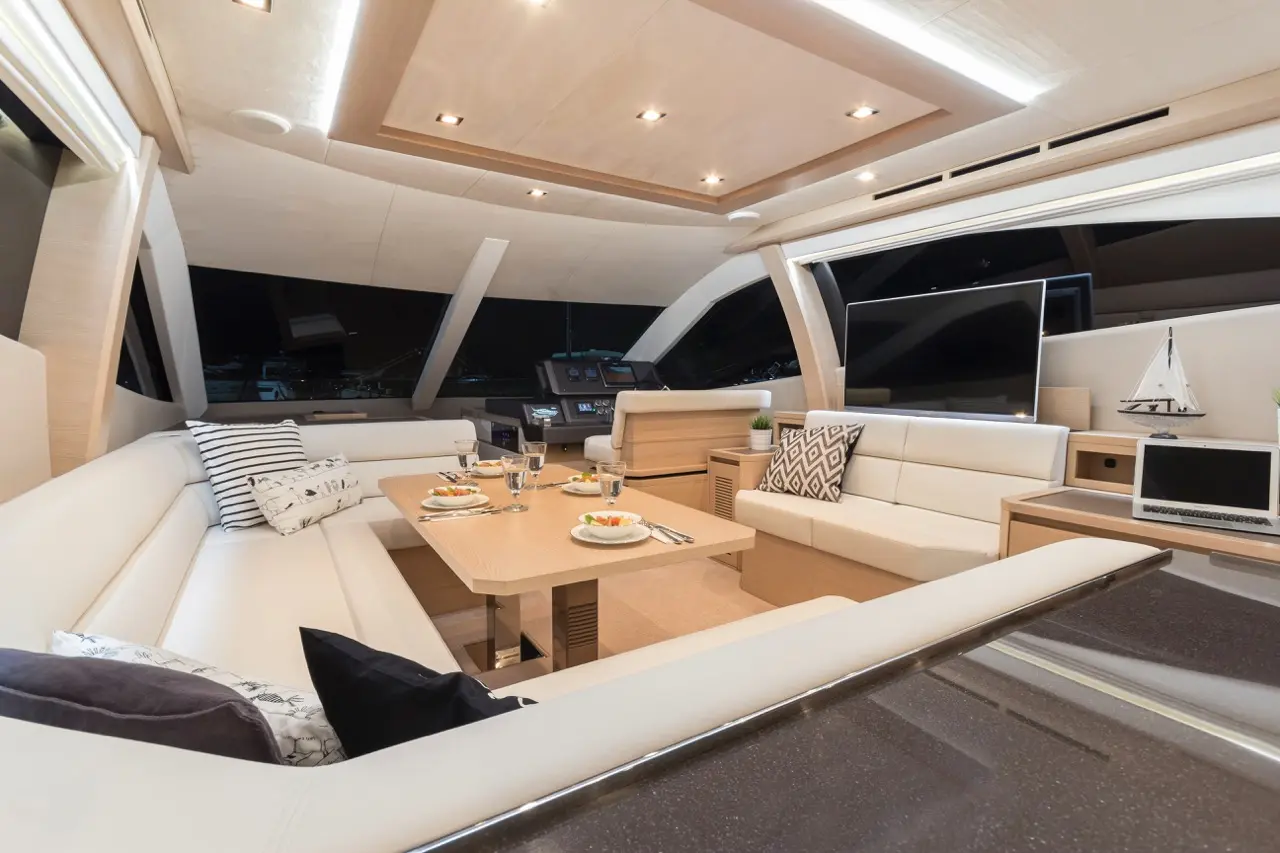 Modern yacht interior with a cozy lounge area, dining table, and large windows overlooking the night sky.