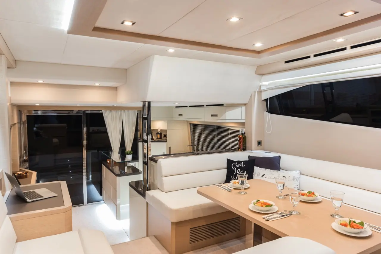 Modern yacht interior featuring a dining area with plated meals, glasses, and a laptop. Bright lighting and elegant decor.