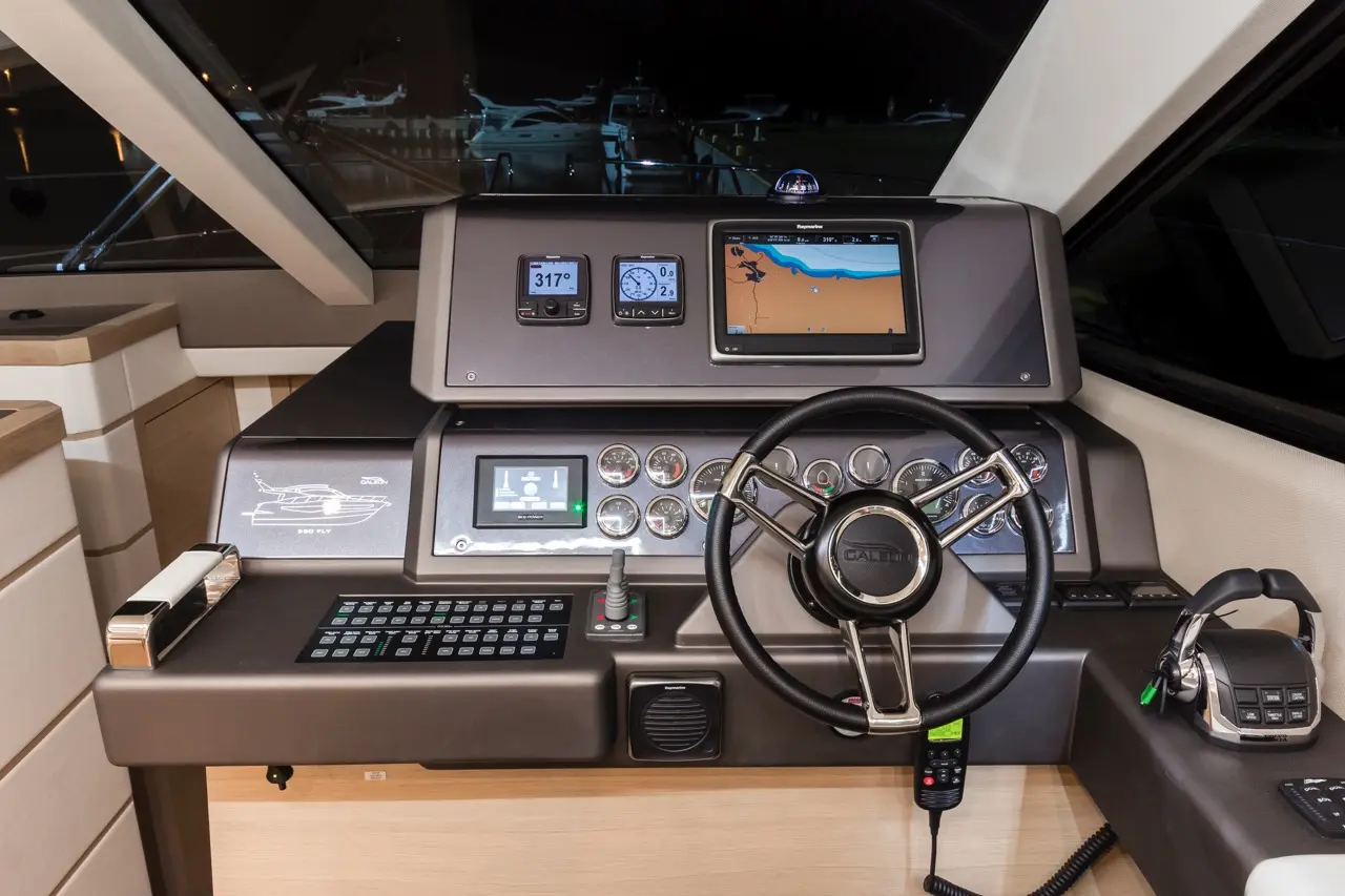 Boat cockpit at night, featuring navigation screens, controls, and steering wheel, showcasing a modern and functional design.