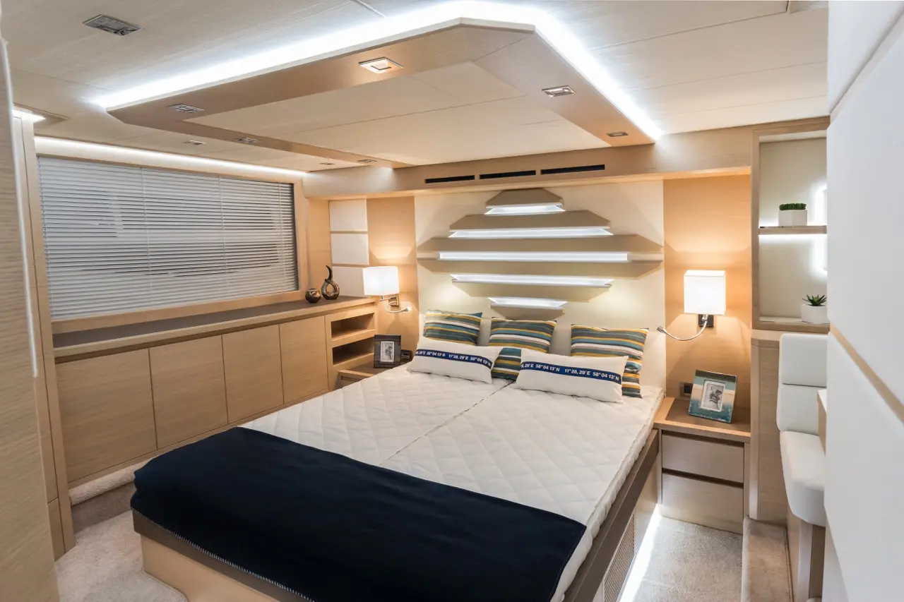Modern yacht bedroom featuring a double bed with striped pillows, sleek wooden cabinets, and soft LED lighting.