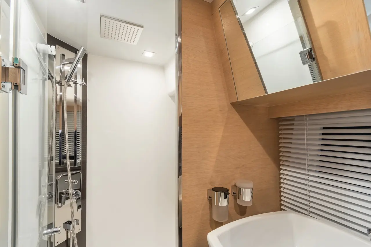 Modern bathroom featuring a glass shower, wooden accents, a white sink, and wall-mounted toiletries.
