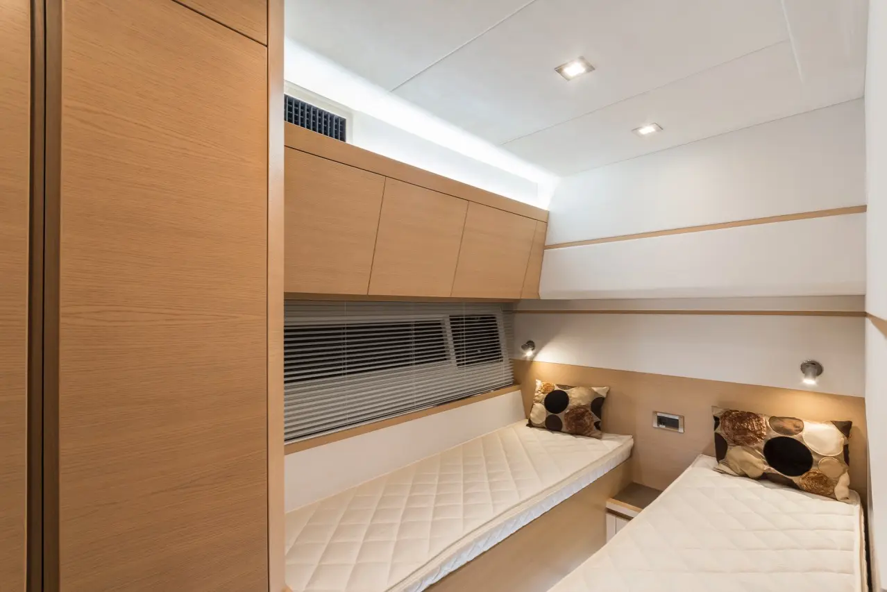 Modern bedroom with two twin beds, wooden paneling, decorative pillows, and overhead storage, featuring soft lighting.