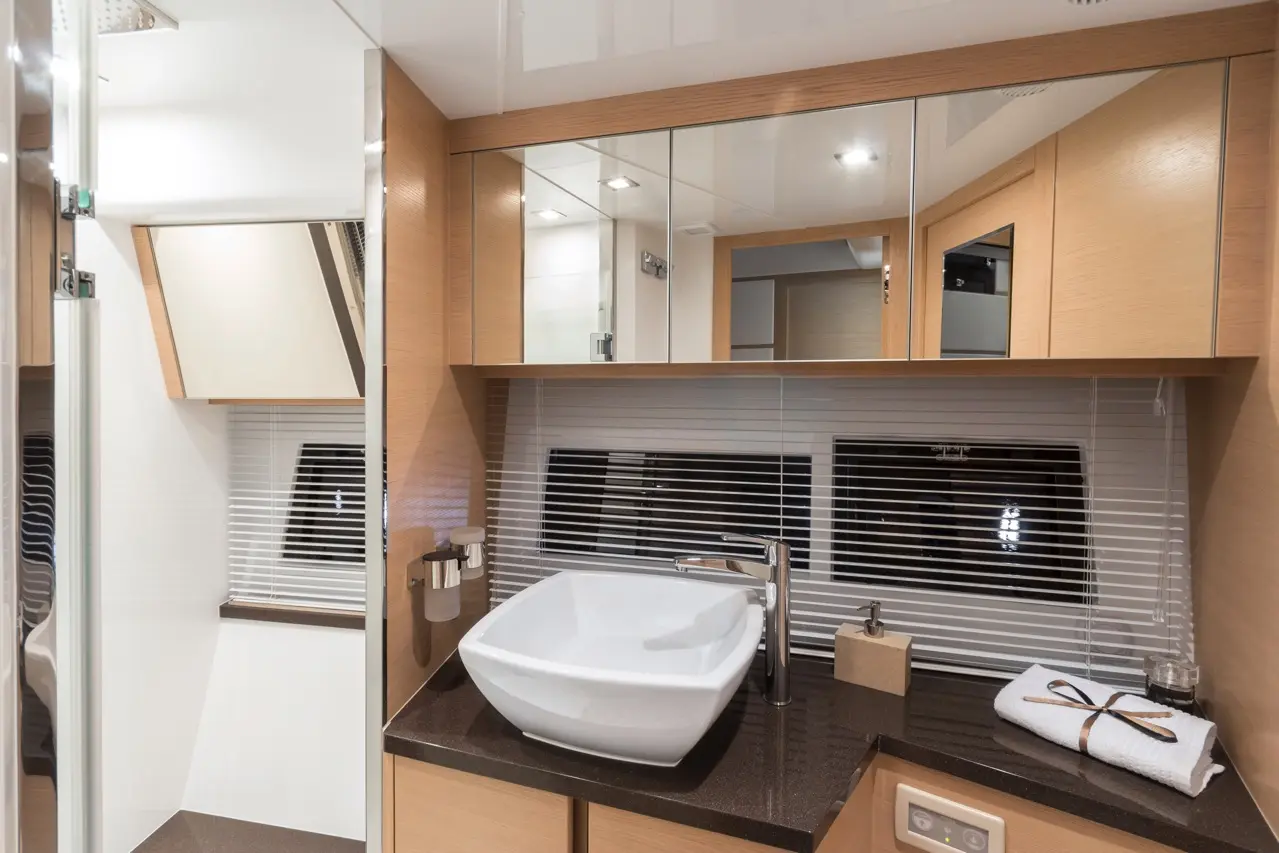 Sleek bathroom with a white ceramic sink, dark countertop, wooden cabinetry, and a window with blinds. Modern design elements visible.