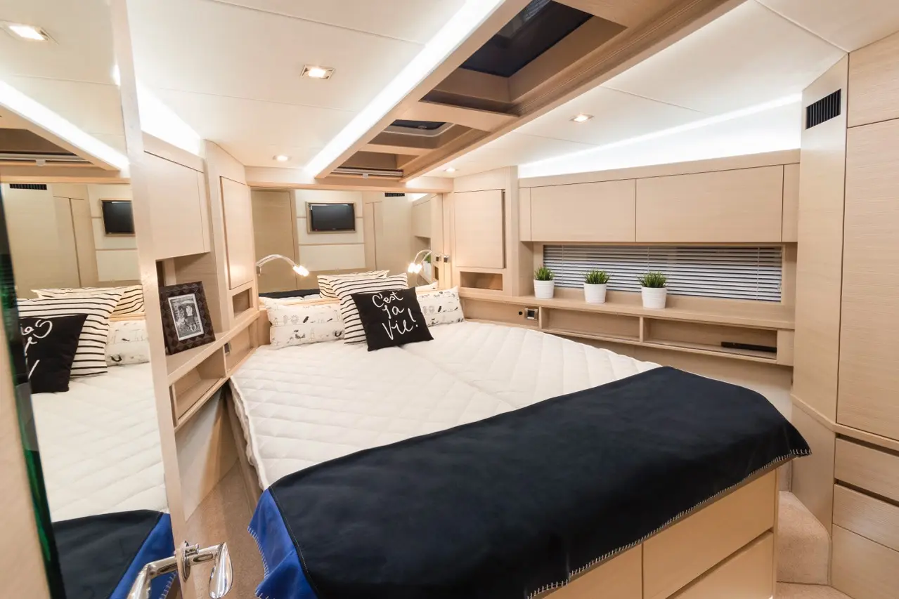 Modern yacht bedroom featuring a queen bed, decorative pillows, overhead lighting, and a wall-mounted TV.