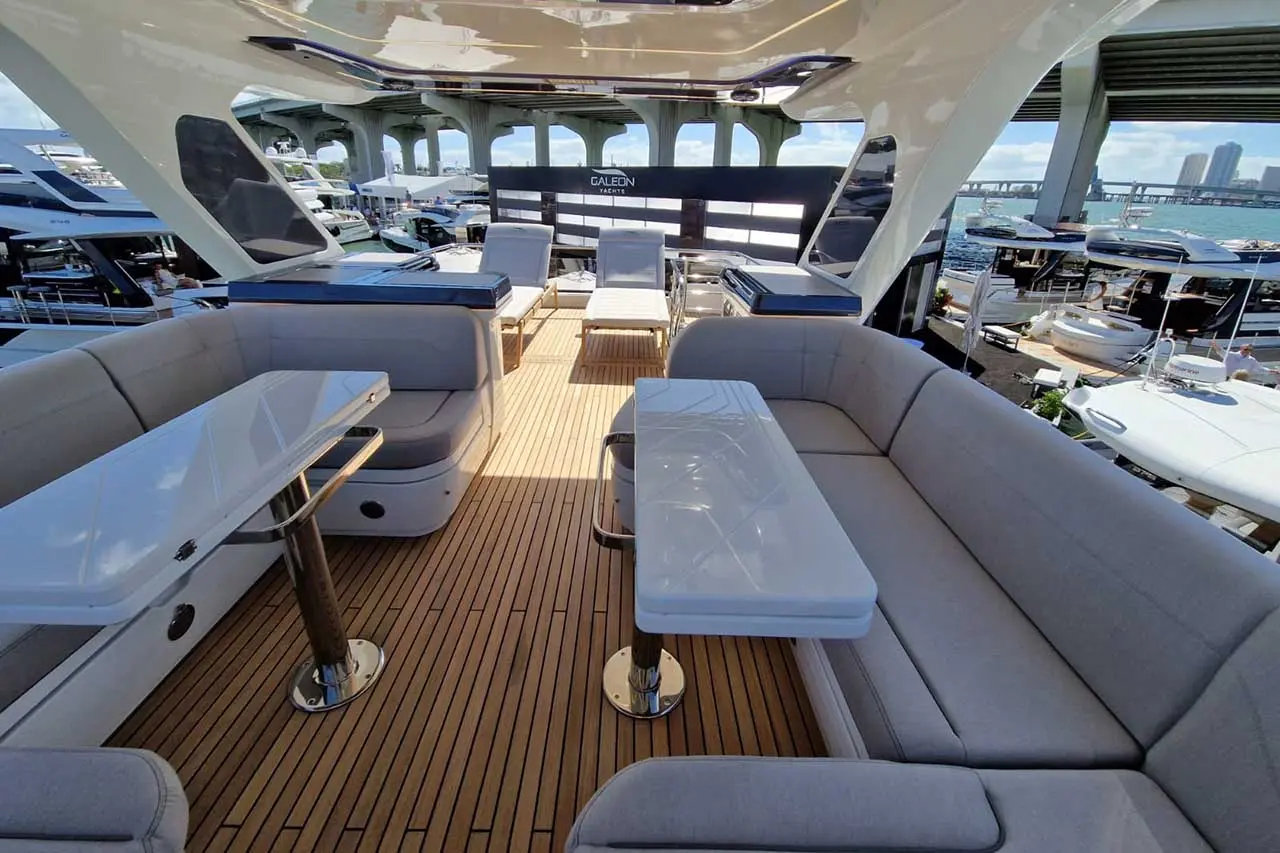 Luxury yacht deck with seating, tables, and sun loungers, featuring a marina view and Galeon Yachts branding in the background.