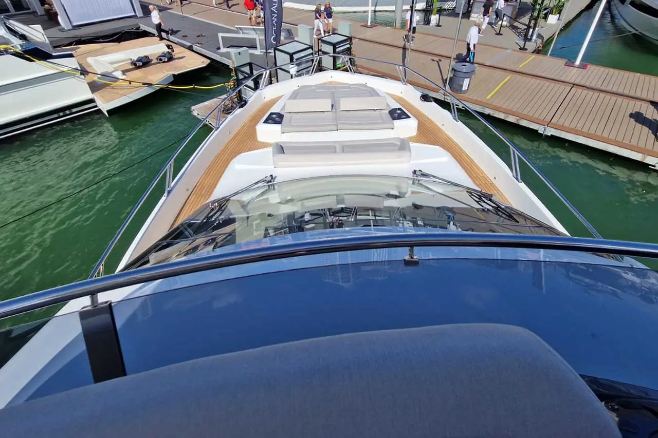 View from the helm of a luxury yacht showing seating area, docks, and people walking by at a marina event.