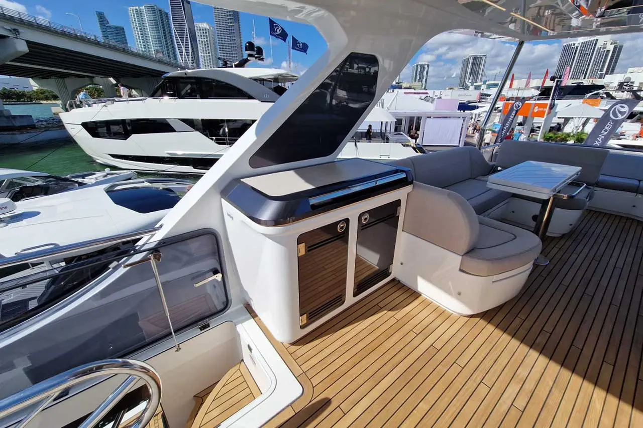 Luxury yacht deck featuring a seating area, table, storage unit, and views of other boats with city skyline in the background.