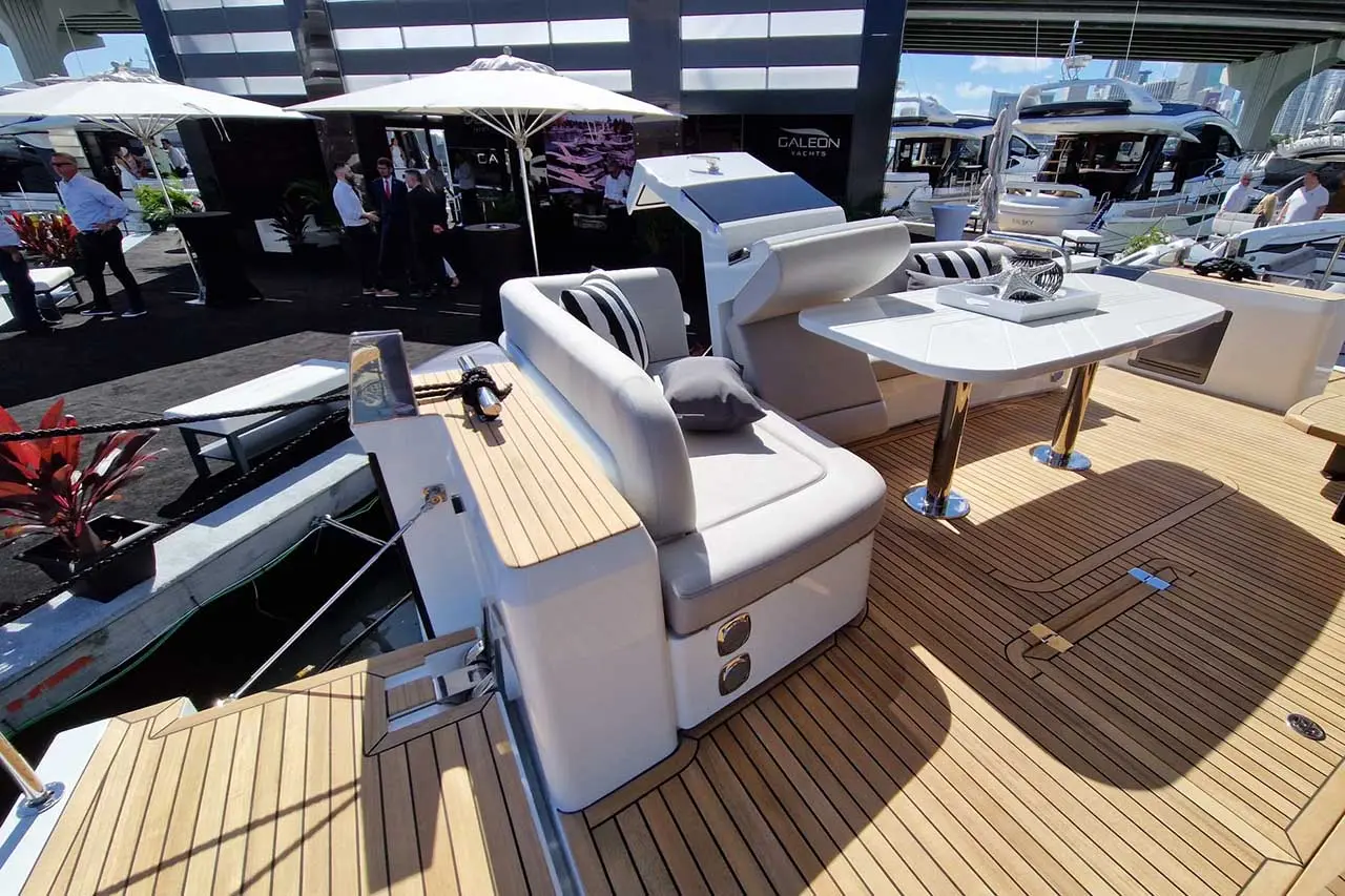 Luxury yacht deck featuring modern seating, a dining table, and ornamental plants under umbrellas, showcasing a sleek design.