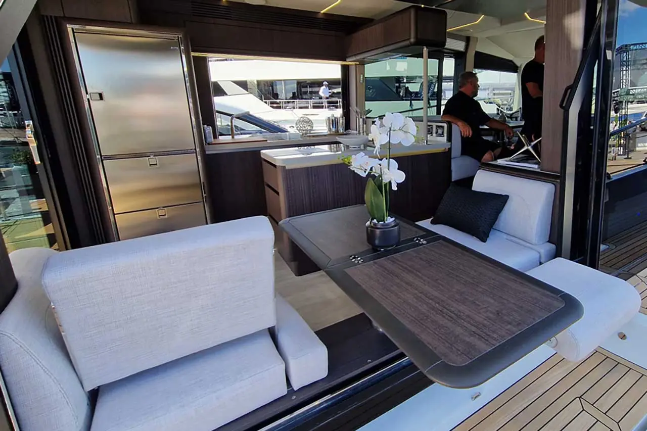 Modern yacht interior featuring a sleek kitchen, seating area, and flower arrangement with crew members in the background.