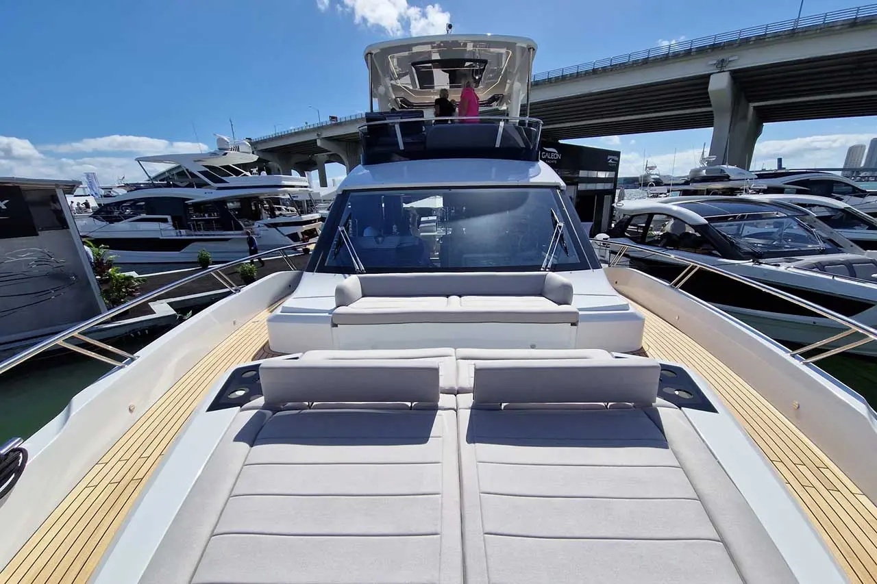 Luxury motor yacht viewed from the front, featuring sunbathing cushions, a sleek design, and other boats in the marina.