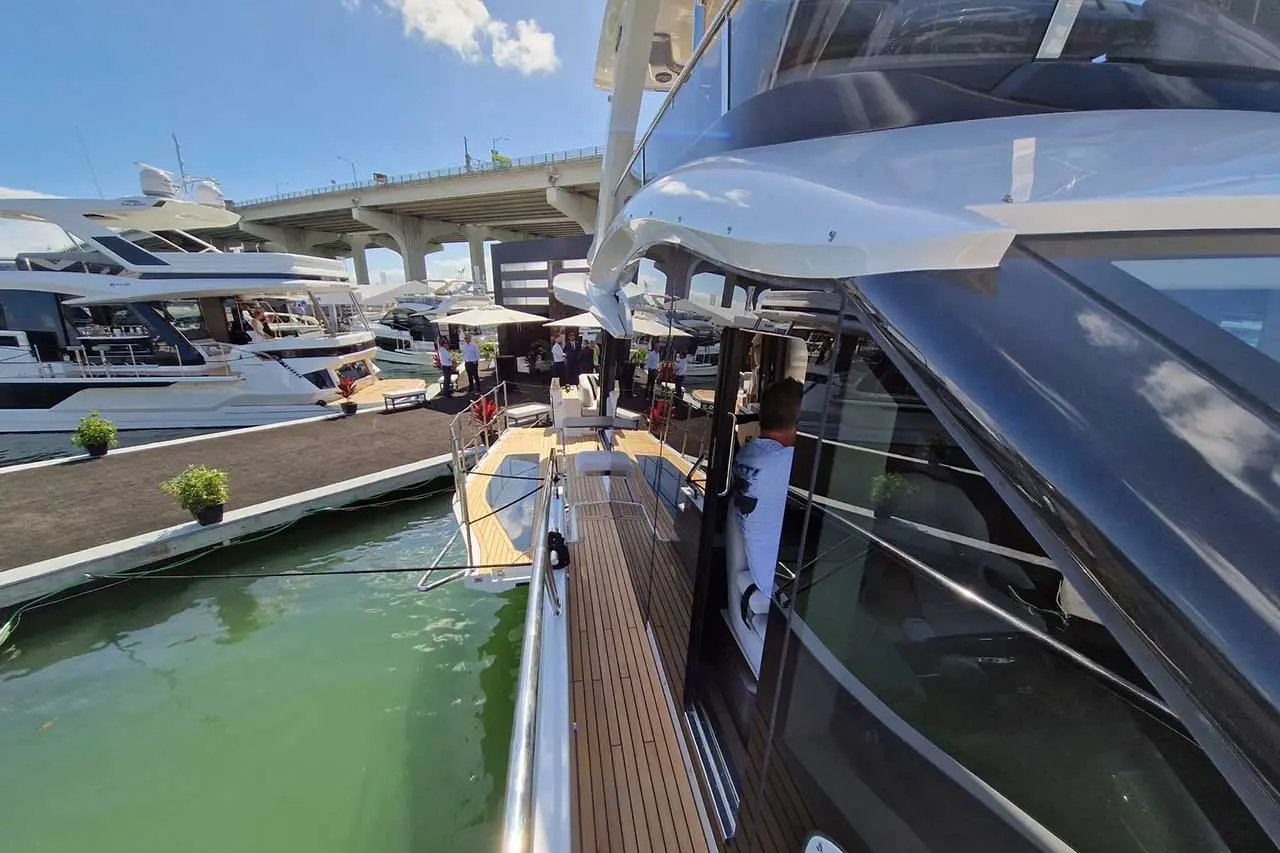 Luxury yacht docked at a marina under a blue sky; people are gathered on the dock, enjoying the boat show atmosphere.