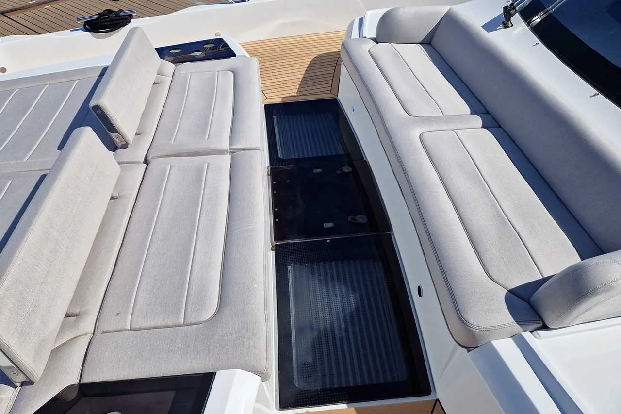 Two gray padded seats on a boat deck, separated by black storage compartments, with wooden flooring in the background.