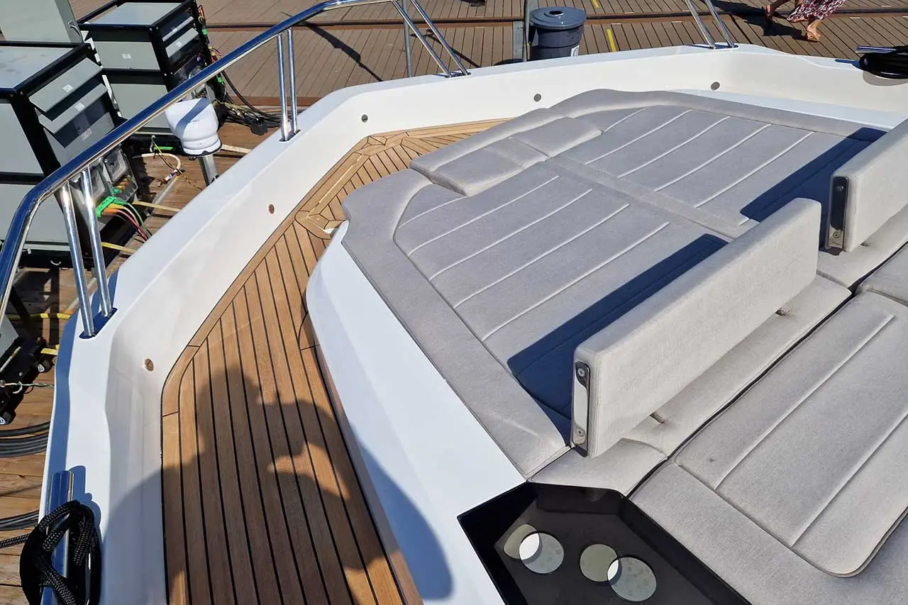 Wide view of a modern boat's deck featuring gray cushioned seating, wooden flooring, and a stainless steel railing.