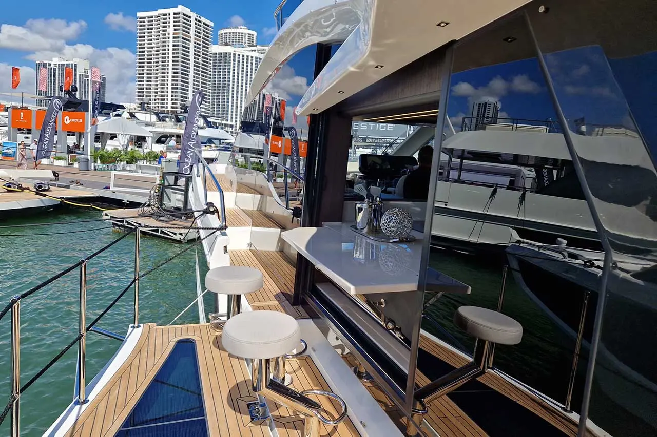 Modern yacht deck showcasing a stylish bar area with stools, overlooking the marina and city skyline under a clear blue sky.