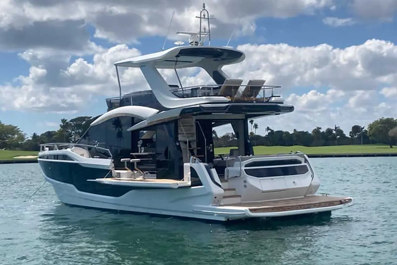 Luxury motor yacht anchored in clear water, featuring a sleek design, outdoor seating, and a scenic green backdrop.