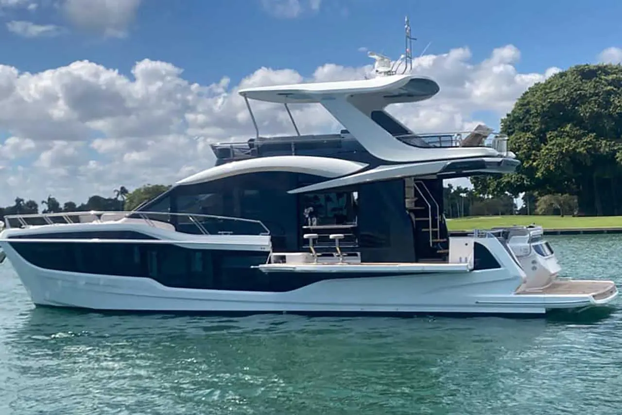 A luxurious, modern yacht with multiple decks and a sleek design, docked in clear water against a sunny sky.