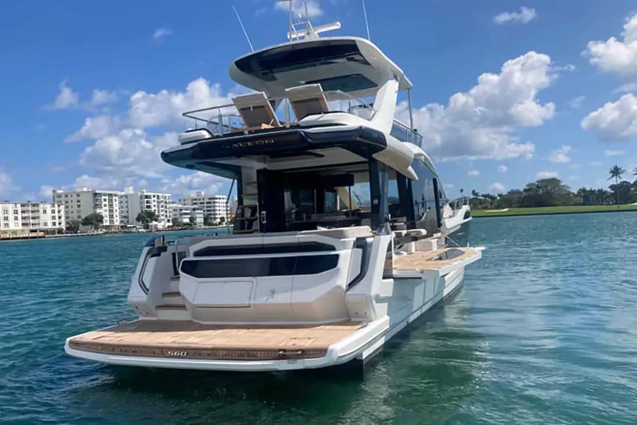 Luxury yacht in calm waters, showcasing sleek design, open deck, and nearby waterfront buildings under a clear blue sky.