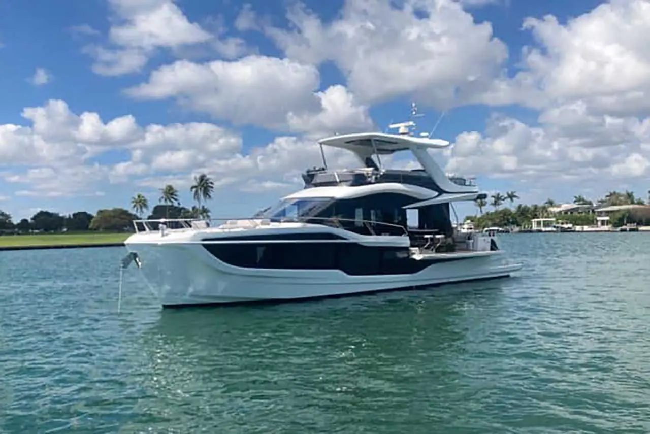 A sleek white yacht anchored in clear blue water, surrounded by palm trees and a blue sky with scattered clouds.